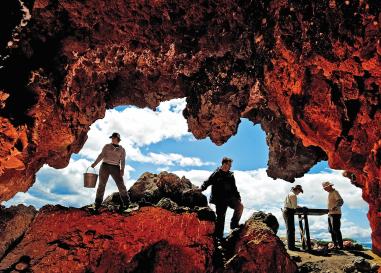 Dramatic opening of a cave with blue sky behind it. Four people are silohouetted in the opening, holding buckets and other tools. 