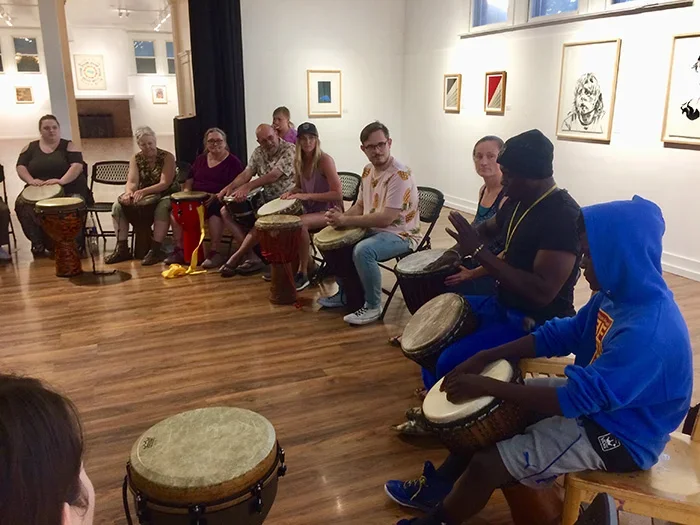 A group of people learn to play drums from a Guinean teacher