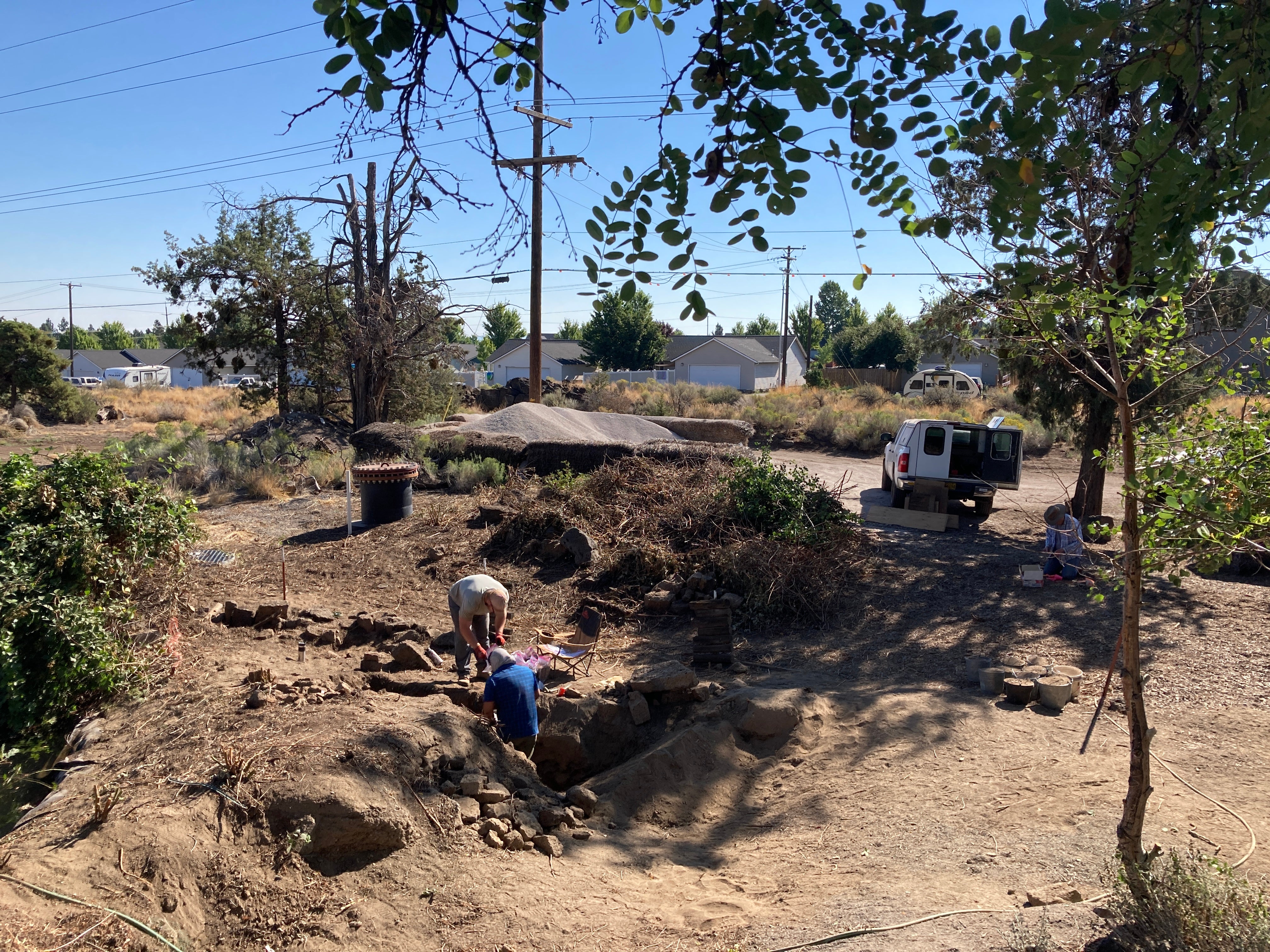 Archaeologists dig in the ground, surrounded by landscaping