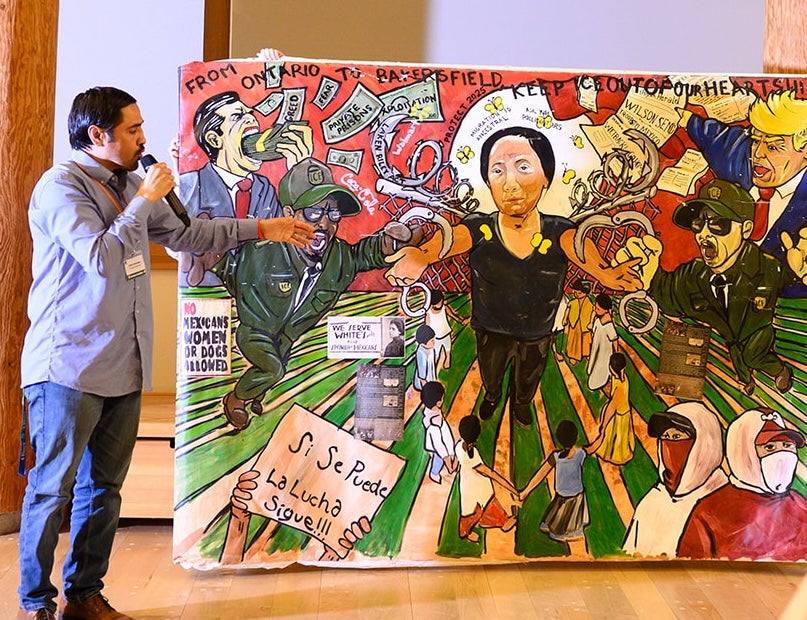 Artist Eddie Melendrez speaks about a mural that he stands next to.