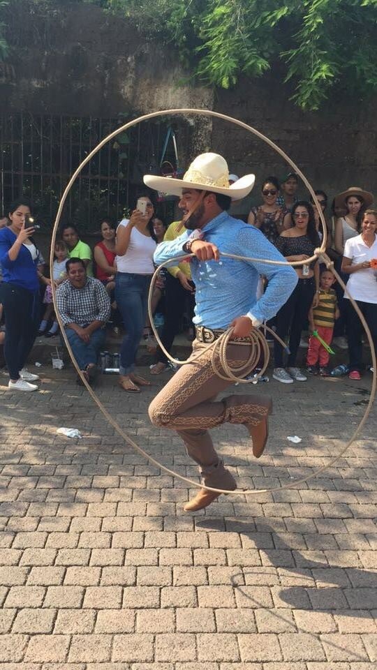 Josue Mendoza performing rope skills for a crowd on the street. He is wearing a blue shirt, white hat, and brown pants.