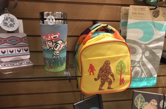 Coasters, a travel mug, a backpack, and a tea towel, all with Pacific Northwest Native motifs. The travel mug features a moose and the backpack features Bigfoot.