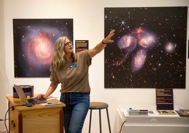 Education Manager Mia Jackson stands in front of two telescope images, presenting training information to museum volunteers.