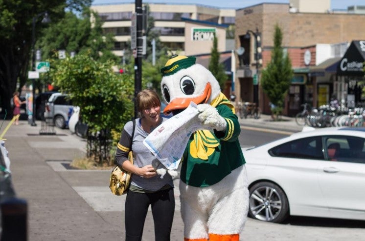 The Oregon Duck holds a map and gives directions to a woman.