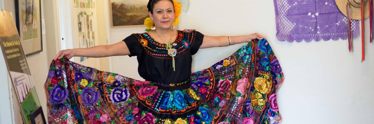 Maria Laguna wearing a colorful Mexican dance dress and spreading out the skirt with her hands.