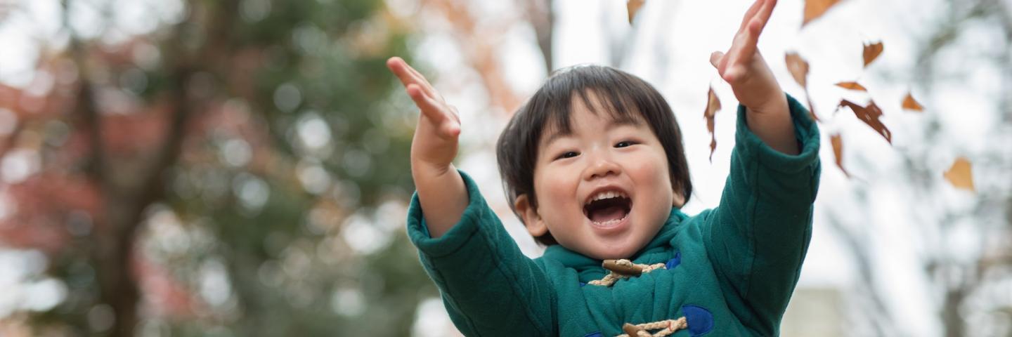 A child with a joyful smile is throwing fall leaves into the air