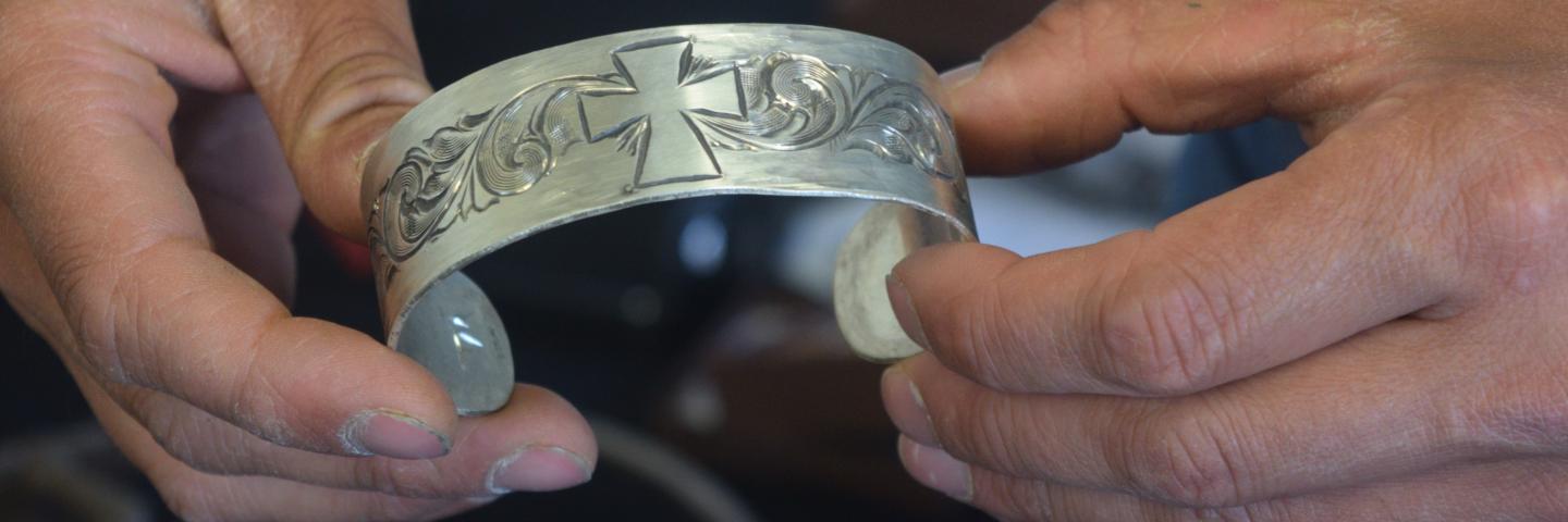 Pat Horlacher holding an intricately carved silver bracelet.