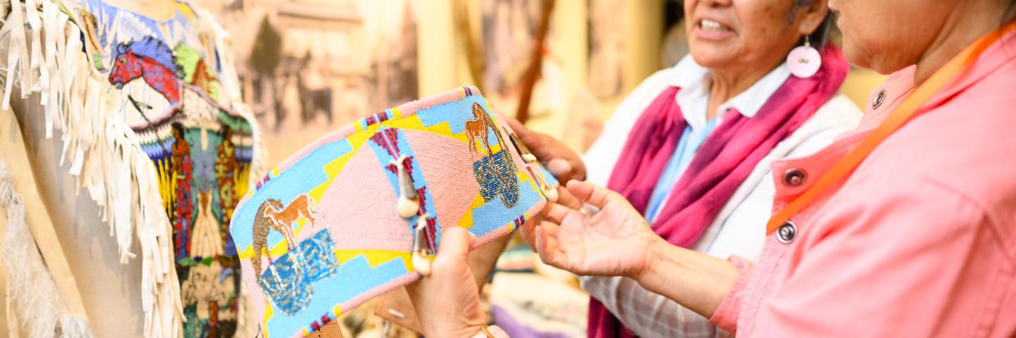 Two women look at a beaded belt.