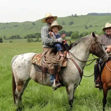Man and small child sit atop a horse in an open field