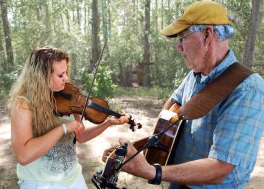 Woman with a fiddle plays next to a man with a guitar
