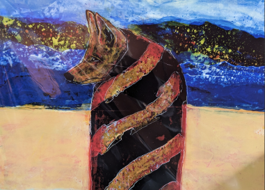 An impressionist-like painting with sand, a river, mountains, and sky. In the foreground is a coyote looking off to the side, wrapped in an orange and blank striped blanket. 