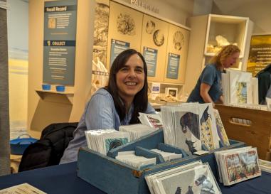 Erika Beyer sits behind a table of her bird prints and smiles at the camera.