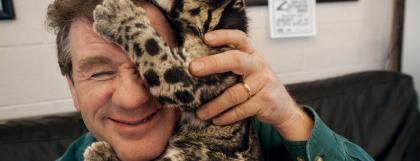 A man holding a leopard cub while it climbs on his head.