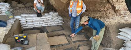 People in field school dig pit with sand bags around them.