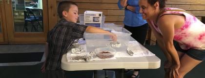 A child plays with the boats activity while two adults look on