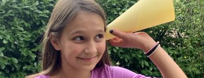 Child holding a funnel up to their ear to test different ways of hearing