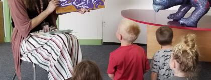 A librarian reads to a group of children while an inflatable triceratops looks on