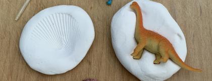 Materials for a dinosaur craft with toy dinosaurs and shells pressed into clay