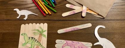 Popsicle sticks, colored pencils, and dinosaur shapes used in a craft project