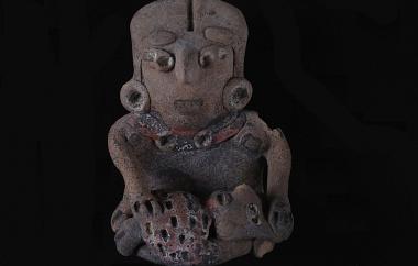 Female Human Figurine Seated with Child on Lap (front). This mother is shown breastfeeding. Her small face holds an animated expression. The baby in her lap is wrapped in swaddling clothes which convey a sense of texture. Buff earthenware, unpolished, traces of red and white paint.