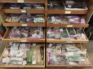 Four rows of wooden drawers are pulled open, overflowing with ziploc bags with artifact information written on them.