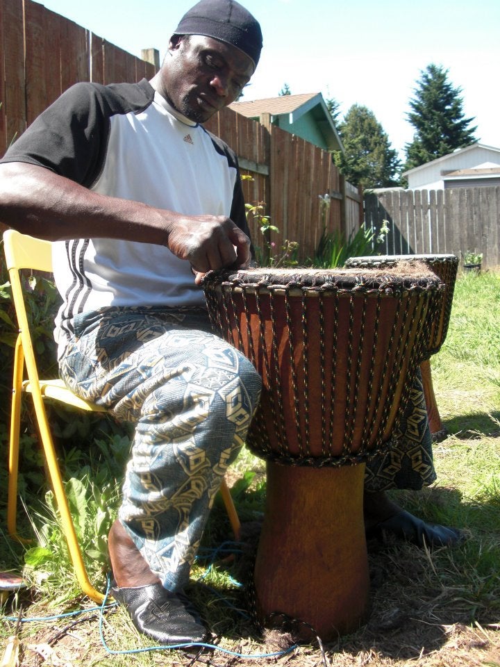 black man in white shirt and patterned pants working on a drum