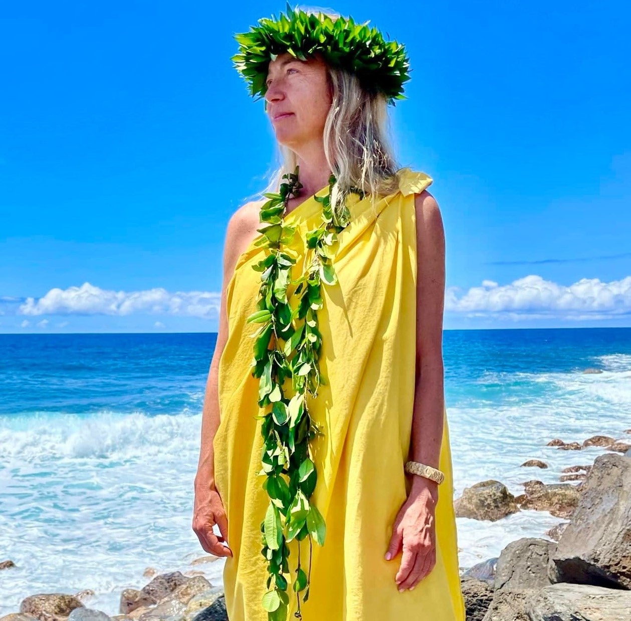 woman in a yellow shirt with a lei and headband by the ocean