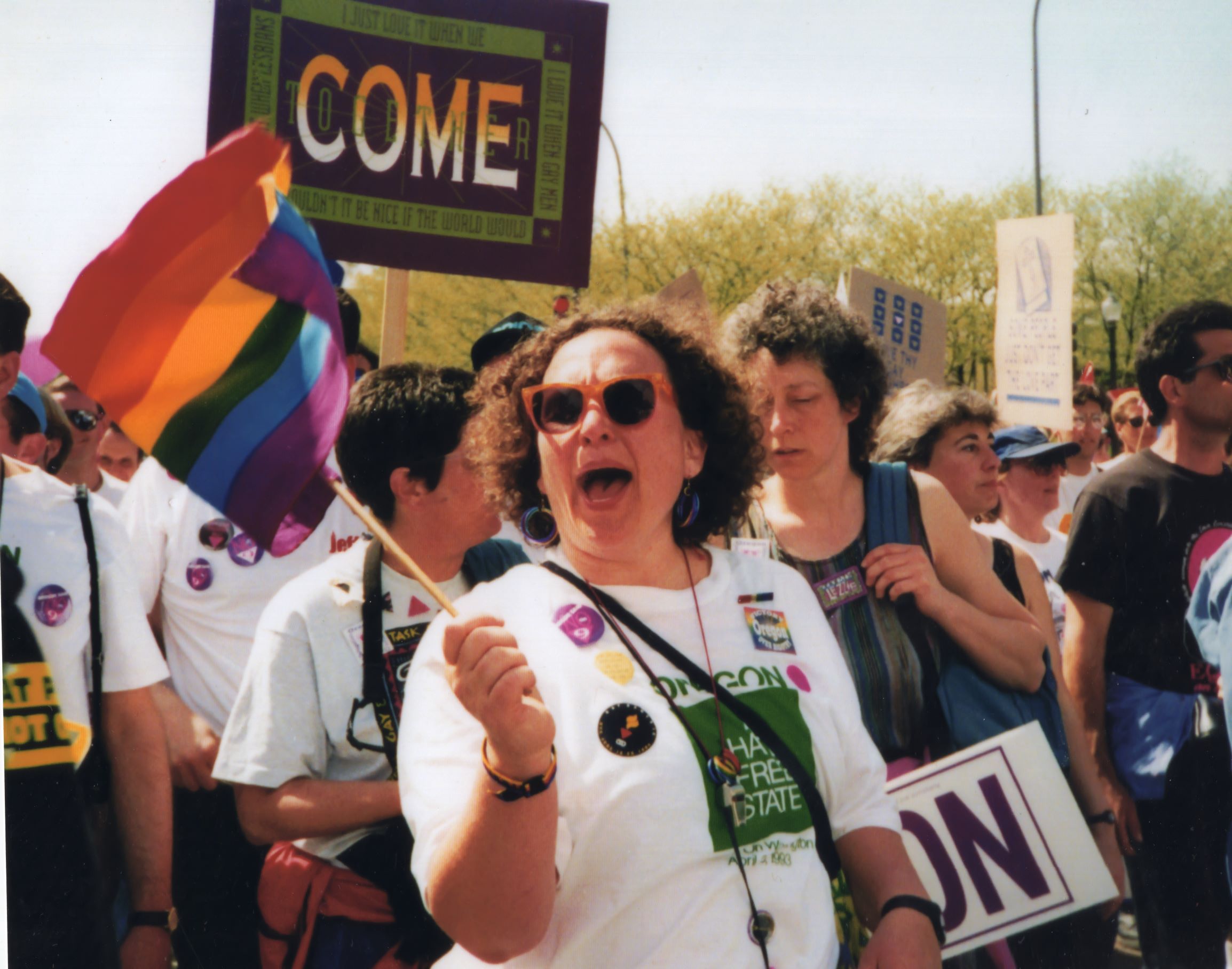 Sally Sheklow marches waving a Pride flag and wearing a "No Hate" shirt