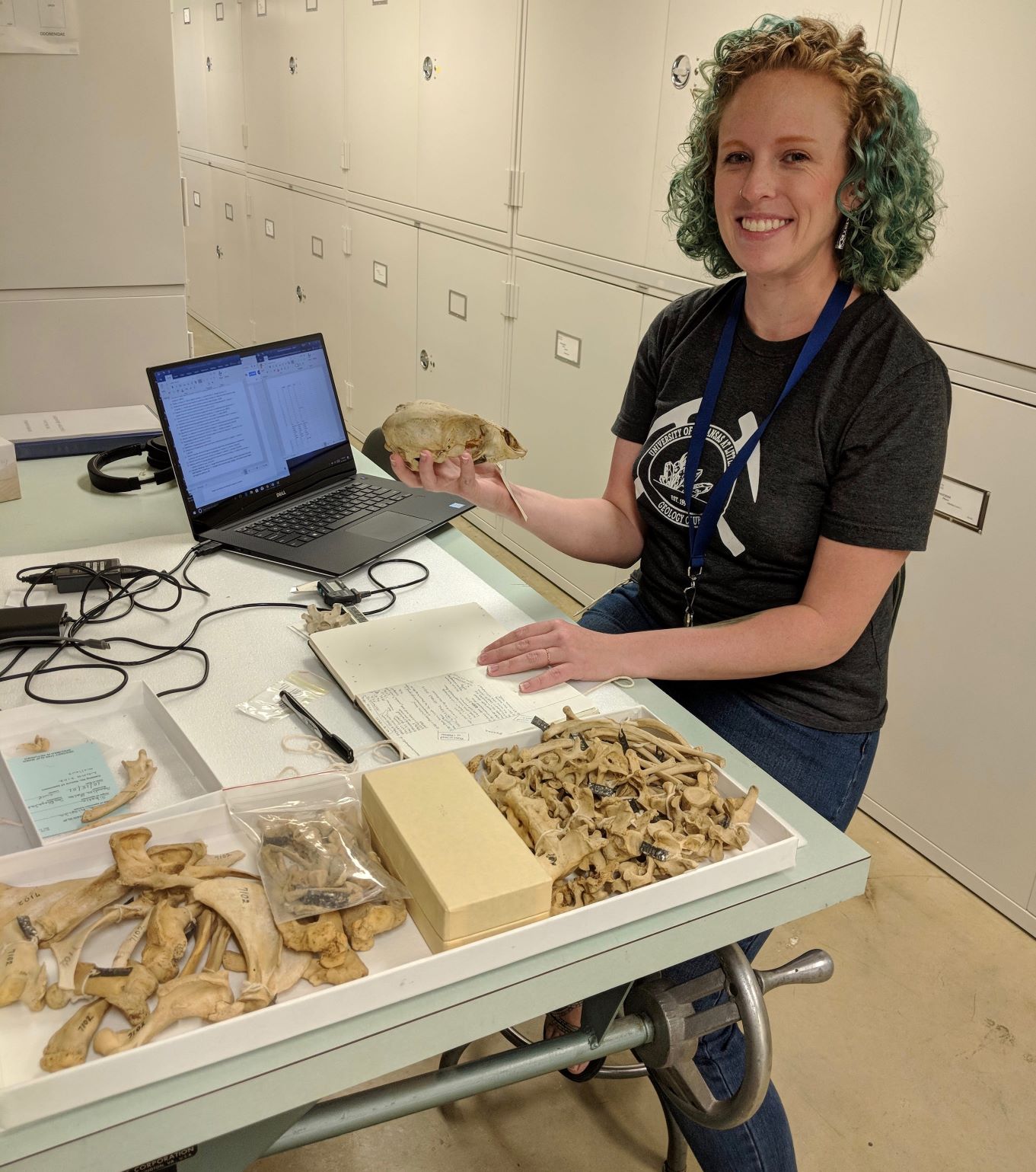 Woman sitting at a table with fossil bones, holding a skull