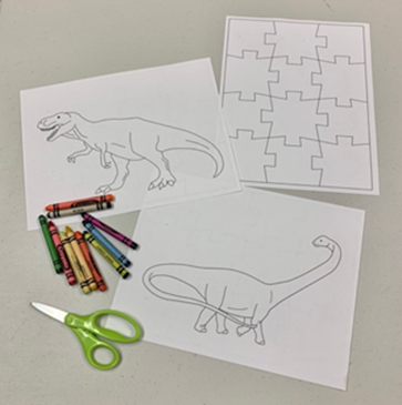 Crayons, scissors, and coloring sheets with dinosarus and puzzle pieces on them. 