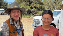 Two women archaeologists hold up their finds. 