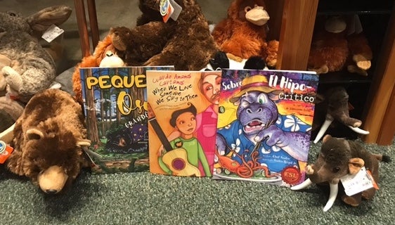 Three childrens' books in Spanish and English sit among plush stuffed animals