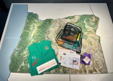 Clear backpack, green vest and activities sitting on a map of Oregon.