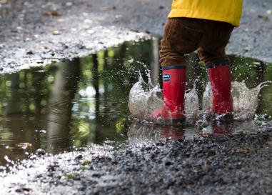 Preschooler jumping in a puddle with red boots