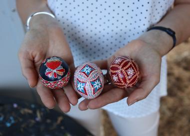 Hands hold intricately decorated and highly colorful eggs--pysanka--in reds, oranges, white, and blue