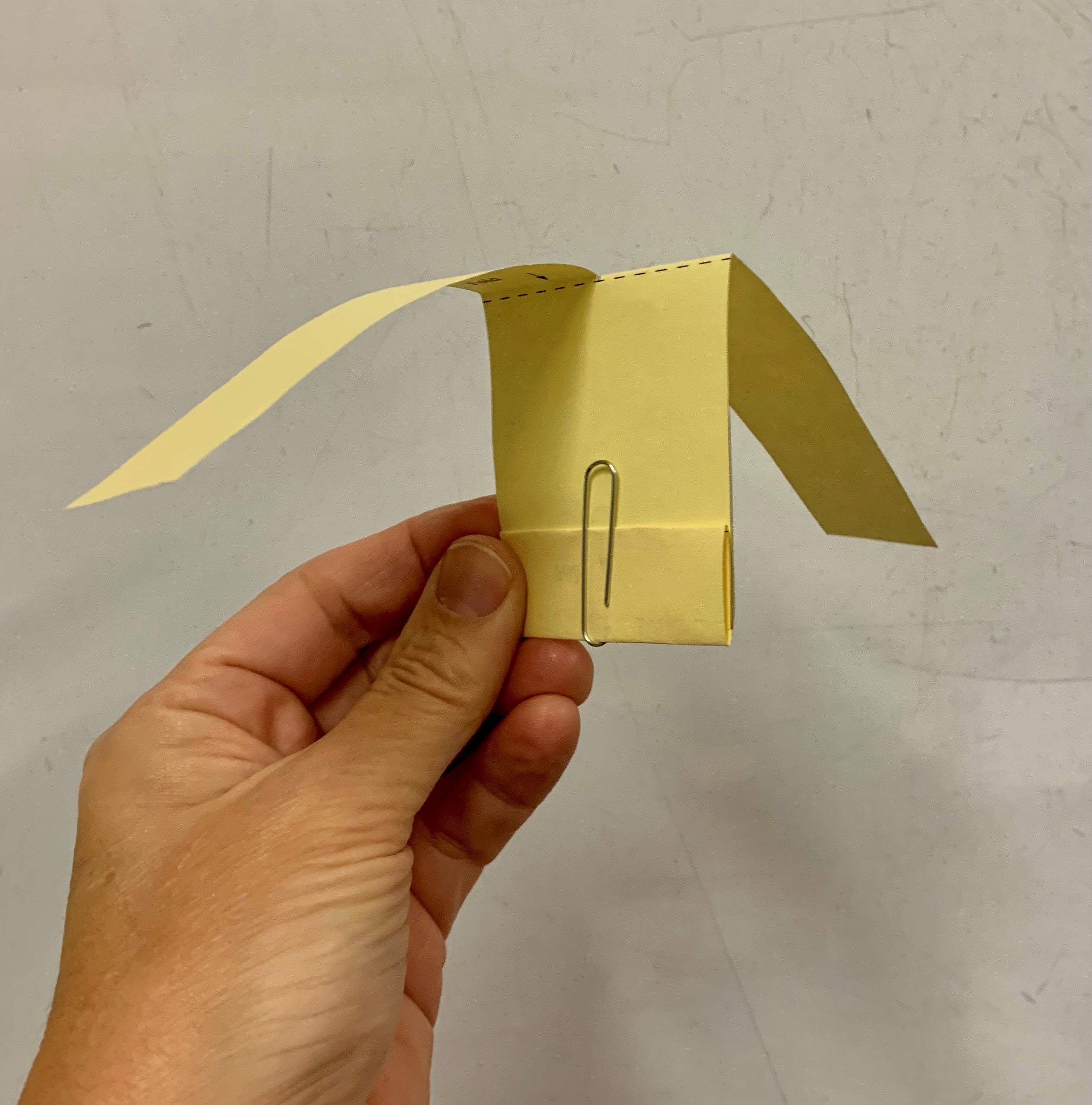 A hand holding a paper helicopter craft.